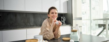 Çekici, genç, neşeli kız mutfakta yemek pişiriyor, para kazanıyor, yemek tarifi kitabını tutuyor, fikirleri var..