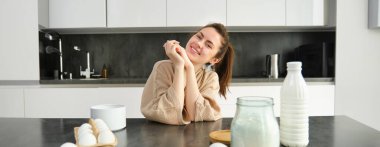 Çekici, genç, neşeli kız mutfakta yemek pişiriyor, para kazanıyor, yemek tarifi kitabını tutuyor, fikirleri var..