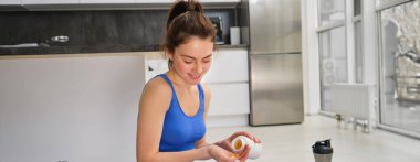 Genç bir kadının görüntüsü, sportif fitness kızı vitamin alıyor, kas gücü için diyet takviyeleri alıyor, yoga minderinde oturuyor ve egzersiz yapıyor..