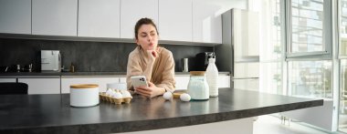 Çekici, genç, neşeli kız mutfakta yemek pişiriyor, para kazanıyor, yemek tarifi kitabını tutuyor, fikirleri var..