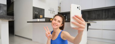 Güzel esmer sporcunun portresi, akıllı telefonda selfie çekmek, cep telefonuyla fitness minderinde poz vermek, spor egzersizlerini kaydetmek, antrenman yapmak..