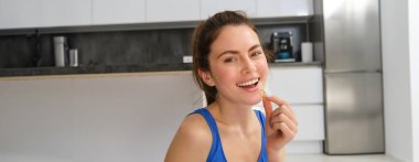 Genç bir kadının görüntüsü, sportif fitness kızı vitamin alıyor, kas gücü için diyet takviyeleri alıyor, yoga minderinde oturuyor ve egzersiz yapıyor..