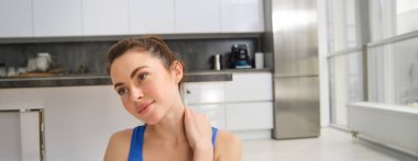 Genç bir kadının portresi evde spor yapıyor, boynuna dokunuyor, antrenmandan sonra omuzlarını ovuyor. Refah ve spor konsepti