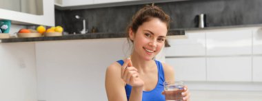 Sağlıklı yaşam tarzı ve beslenme. Gülümseyen, beslenme destek tomurcukları ya da vitaminler alan, idmandan sonra balık yağı kullanan, kameraya mutlu bakan genç bir kadın..
