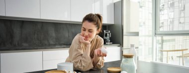 Çekici, genç, neşeli kız mutfakta yemek pişiriyor, para kazanıyor, yemek tarifi kitabını tutuyor, fikirleri var..