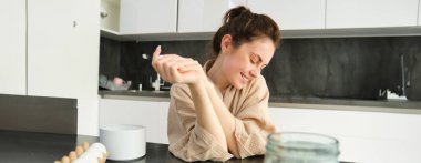 Çekici, genç, neşeli kız mutfakta yemek pişiriyor, para kazanıyor, yemek tarifi kitabını tutuyor, fikirleri var..