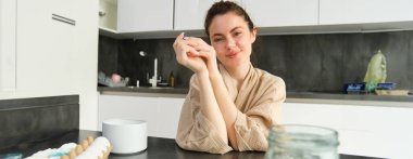 Çekici, genç, neşeli kız mutfakta yemek pişiriyor, para kazanıyor, yemek tarifi kitabını tutuyor, fikirleri var..