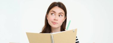 Esmer genç bir kadının portresi, yaratıcı kız düşünen, elinde kalem ve defter tutan, not alan, günlüğüne yazan, beyaz arka planda duran.