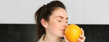 Bornozlu güzel esmer kadının portresi, portakal suyuyla poz veriyor, taze meyve suyu hazırlıyor, sağlıklı bir yaşam sürüyor, sabahına vitamin içeceği ile başlıyor..