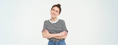 Gülümseyen bir kadının portresi, göğsünde çapraz kollar, düşünceli bir yüzle yana bakıyor, düşünüyor, seçim yapıyor, bir şeyler hayal ediyor, beyaz arka planda duruyor..