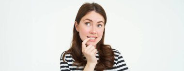 Meraklı genç bir kadının portresi, parmağını ısırır ve düşünceli bir şekilde yukarı bakar, karar verir, yemek seçer, beyaz arka planda durur..