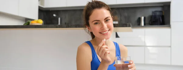 stock image Close up portrait of brunette fitness woman, taking dietary supplements, vitamins and glass of water after workout at home.