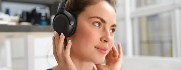 Close up portrait of fitness woman, smiling and listening music, wearing wireless black headphones.