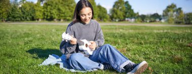 Kaygısız Asyalı kız parkta ukulele çalıp şarkı söylüyor, çimlerin üzerinde oturuyor, müzisyen boş zamanlarında dışarıda dinleniyor..
