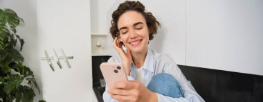 Evde cep telefonuyla oturan bir kadının portresi, akıllı telefon uygulaması üzerinden online alışveriş, içeride zaman geçirmek..