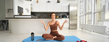 Gülümseyen kız atlet, spor kadın aktif giyimde yoga yapıyor, nilüfer pozisyonunda yoga minderinde oturuyor, meditasyon yapıyor, farkındalık egzersizleri yapıyor..