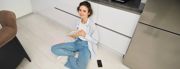 Stock image Top angle view of girl student studying at home. Young woman sitting on floor with journal, writing in her planner, reading notes in notebook.