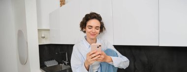 Evde cep telefonuyla oturan bir kadının portresi, akıllı telefon uygulaması üzerinden online alışveriş, içeride zaman geçirmek..
