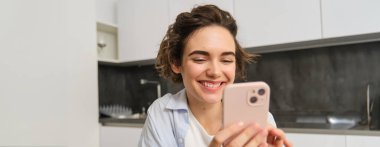 Evde güzel bir kadının portresi, elinde akıllı telefon, cep telefonu uygulamasından online alışveriş..