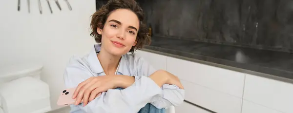 stock image Portrait of young beautiful woman feeling cozy at home, sitting in kitchen and smiling, enjoying spending time indoors.