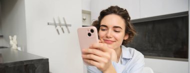 Evde oturup cep telefonunu kontrol eden mutlu bir gülümsemeyle akıllı telefona bakan bir kadının portresi..