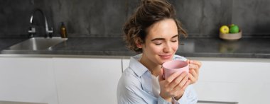 Mutlu sabahlar. Mutlu esmer kadının portresi, mutfağında bir fincan kahve içiyor ve gülümsüyor, günün sıcak ve sıcak bir başlangıcında çay içiyor..