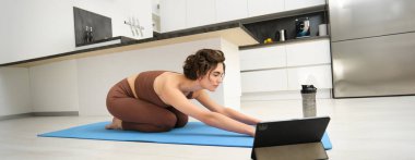Genç bir sporcunun evde yoga yapması, tablet üzerinde beden eğitimi videosu izlemesi, vücut esnemesi, beden eğitimi alıştırmaları, evdeki pilates dersleri..