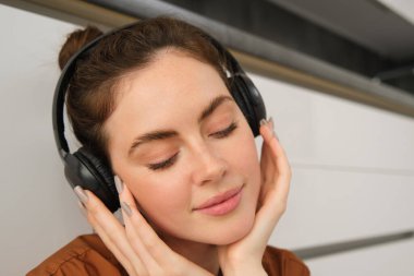 Modern bir kadın tasviri, güzel bir kız müzik dinlemeyi seviyor, siyah kablosuz kulaklıkları var, yerde oturuyor ve dinleniyor..