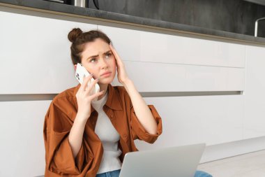 Doktorunu telefonla arayan, elinde akıllı telefon tutan, kaşlarını çatan ve kafasına dokunan bir kadının portresi, ağrılı bir baş ağrısı veya migreni var, kendini kötü hissediyor..