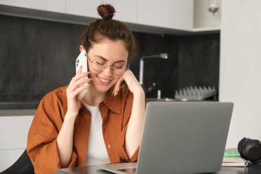 Serbest çalışan genç bir kadının portresi, evden çalışan bir girişimci, serbest çalışan bir müşterinin. Sipariş veren, telefonla konuşan, mutfakta dizüstü bilgisayarla oturan bir kız..