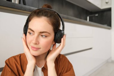 Modern bir kadın tasviri, güzel bir kız müzik dinlemeyi seviyor, siyah kablosuz kulaklıkları var, yerde oturuyor ve dinleniyor..