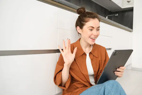 Portrait of woman saying hello, waving hand at digital tablet, connects to video chat, studying online on remote using her device to connect to the class.
