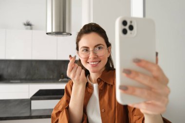 Güzel genç bir kadın, sosyal medya blogcusu video kaydı, online video sohbeti akıllı telefondan, cep telefonuyla evde duruyor..