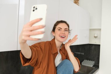 Hevesli tatlı kız mutfak tezgahında fotoğraf çekiyor, akıllı telefon uygulamasında selfie çekiyor..