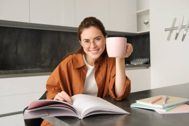Mesafe öğrenme. Evde okuyan, çay içen, çalışma kitabını okuyan, sınava hazırlanan genç bir kadın..
