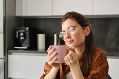 Dinlenen genç bir kadının portresi, çay içen. Kız mutfakta çay içiyor, elinde kupa tutuyor ve düşünceli görünüyor..