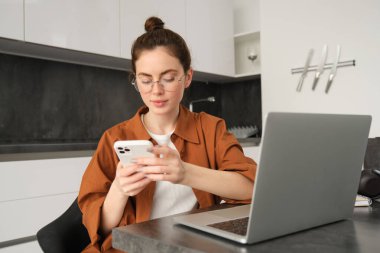 Serbest çalışan genç bir kadının portresi, dizüstü bilgisayarla çalışan bir kadın, mutfakta bilgisayarla oturan bir kız programcı, akıllı telefondan gelen mesaja cevap veriyor..