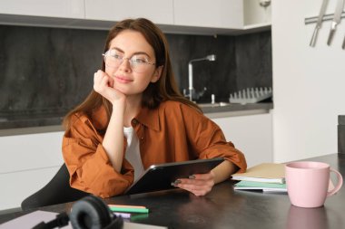 Evden çalışan genç bir kadının portresi, dijital tablet dersine bağlanmak, gözlük takmak, mutfağında uzaktan eğitim, uzaktan öğrenme ve eğitim kavramı..