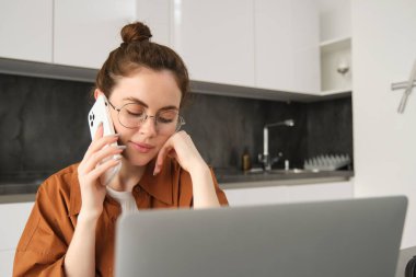 Bilgisayardan alışveriş yapan, bilgisayarla çalışan, telefonla konuşan, gülümseyen, müşteriyle konuşan, uzaktan kumandayla çalışan genç bir kadının portresini kapat..