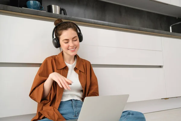 Image of young woman, programmer, freelancer working form home, sitting in headphones and using laptop.