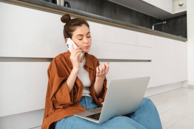 Yerde oturup sohbet dinlerken sıkılmış ve keyifsiz görünen bir kadın dizüstü bilgisayarı kucağında, sırada bekliyor, telefon görüşmesi yapıyor..