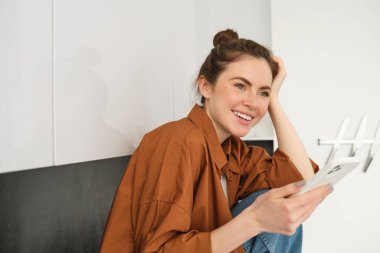 Cep telefonlu genç bir kadının portresi, sosyal medyaya göz atmak, online alışveriş, mutfak tezgahında oturmak, gülümsemek ve mutlu görünmek..