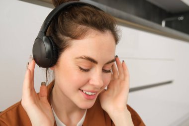 Güzel esmer kadının yakın portresi, kablosuz kulaklıkla müzik dinliyor, kafasında yeni kulaklıklar var, gülümsüyor ve mutlu görünüyor..