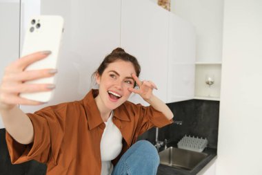Genç karizmatik kız mutfakta fotoğraf için selfie çekiyor, cep telefonunu uzatarak tutuyor..