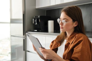 Genç ve güzel bir kadının evde vakit geçirmesi, gözlüklerle dijital tablet okuması, mutfakta oturması..