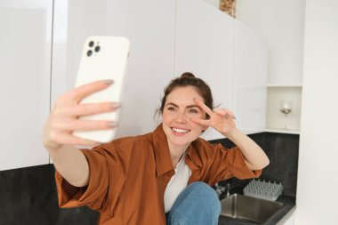 Güzel genç bir kadının portresi akıllı telefonuyla resim çekiyor, fotoğraflara poz veriyor, kendi için filtre uygulaması kullanıyor..