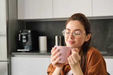 Güzel bir genç kadının portresi, fincandaki kahvesinin kokusu, bardak içmesi, mutfakta oturması..