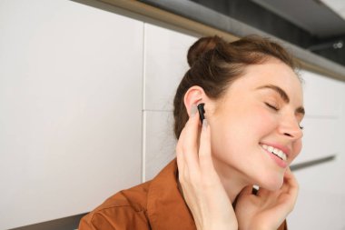 Kablosuz siyah kulaklıklarıyla ses kalitesinden gülümseyen, kulaklıkla müzik dinleyen kadın portresini yakından çekerken memnuniyet dolu yüzü ve gözleri memnuniyetten kapalıdır..