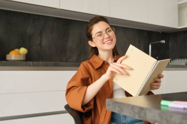 Gözlüklü güzel bir kadının portresi, kolejli bir kız gülümsüyor, mutfakta dizüstü bilgisayarla oturuyor..