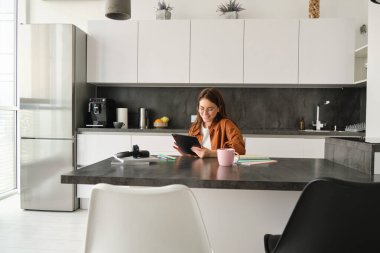 Genç bir kadının portresi, mutfakta elinde tablet ve defterle oturan, internette haber okuyan, uzaktan eğitim alan, evde e-öğrenim gören bir öğrenci..